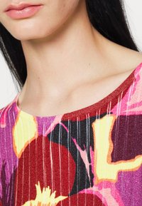 Pestrý ribovaný top s květinovým vzorem v odstínech růžové, žluté a černé, s kulat�ým výstřihem a lehkou texturou.