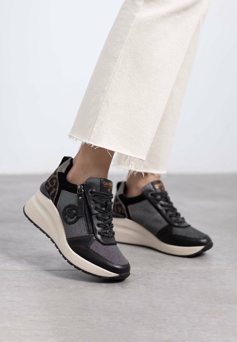 Baskets noires et grises en matériaux mélangés, avec une accent en imprimé léopard, semelle épaisse beige et design à lacets. Détail de fermeture éclair sur le côté visible.