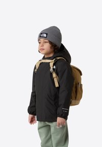 Juoda neperšlampama striukė su kapišonu, smėlio spalvos kuprinė, pilka kepurė, ir mėtų spalvos kelnės; turi reguliuojamas dirželes ir logotipo dekoro elementus.