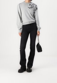 Grå sweatshirt med bladmønster på den ene skulder, parret med sorte flairbukser og chunky sorte sko. Lille sort håndtaske med kædetræksrem.