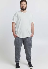 Hvid v-hals t-shirt kombineret med mørkegrå, teksturerede joggerbukser. Modellen står afslappet med hænderne i lommerne iført sorte sneakers.