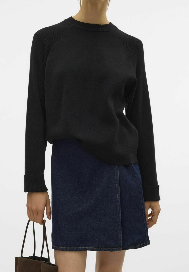 Czarny sweter z długim rękawem i raglanowymi rękawami, połączony z ciemnoniebieską dżinsową spódnicą. Stylizacja charakteryzuje się prostym wzornictwem i teksturowanym materiałem.