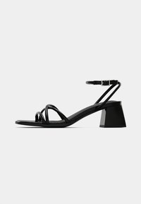 Black heeled sandals with sleek straps featuring a block heel, smooth texture, and an adjustable ankle buckle. Flat sole for stability.