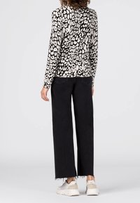 Haut à manches longues en imprimé léopard noir et blanc, associé à un pantalon large taille haute noir. Baskets blanches à semelle épaisse.