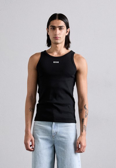 Débardeur noir sans manches avec le logo blanc "MSGM" sur la poitrine, en tissu côtelé. Associé à un pantalon en denim bleu clair.