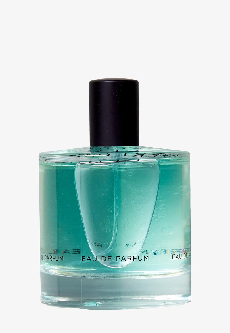 Bottiglia di profumo in vetro trasparente con liquido turchese e tappo nero, etichettata "Eau de Parfum" su sfondo bianco.