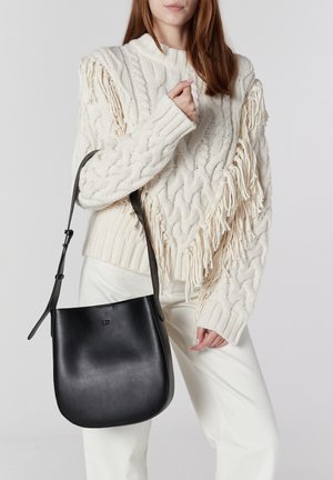 Borsa a tracolla in pelle nera con base arrotondata e tracolla regolabile, abbinata a un maglione crema in maglia a treccia con dettagli in frange.