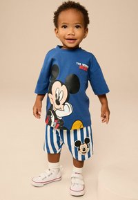 Blå kortærmet T-shirt med Mickey Mouse grafik. Stribede blå og hvide shorts med Mickey ikon. Hvide sko med røde detaljer.