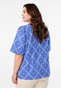 Kurzärmlige blaue Bluse mit weißem geometrischen Muster. Aus leichtem Stoff gefertigt, mit einer lässigen Passform und Rundhalsausschnitt.