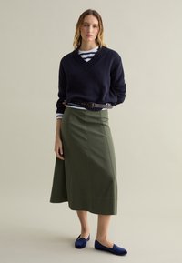 Navy knitted sweater with v-neck, green knee-length skirt, and dark blue flats. Striped shirt serves as an underlayer with a black belt.