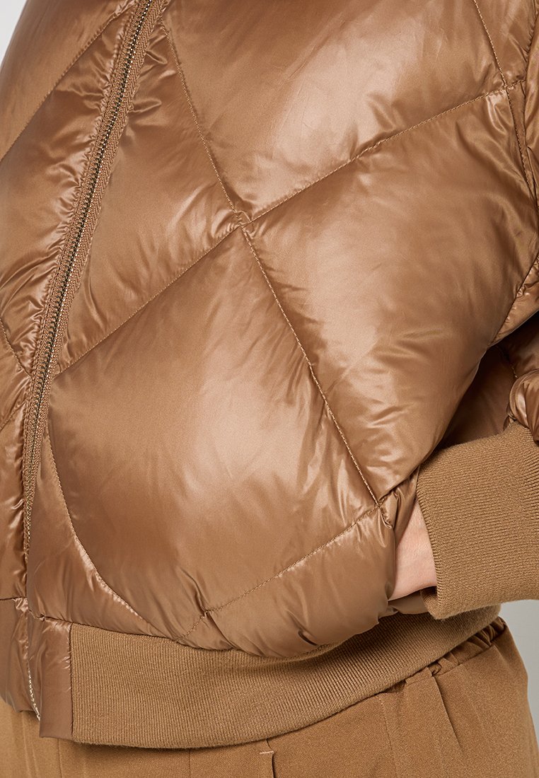 Brązowa kurtka puchowa o błyszczącej, pikowanej teksturze, z ukośnym wzorem, zamek błyskawiczny oraz ribbowe mankiety w pasującym odcieniu.