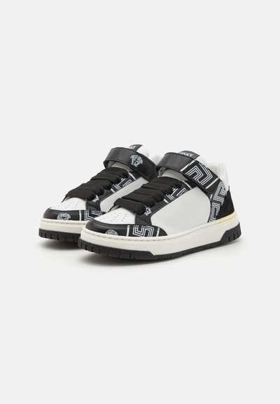Svartvita sneakers med en slät läderöverdel, tryckt mönster och kardborreband. Har en strukturerad svart sula och en vadderad tunga.