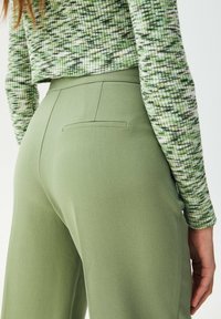 Pantalon vert à texture lisse, doté d'une poche arrière unique et d'une taille haute, assorti à un pull en maille vert à motifs.