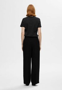 Schwarz-weiß gestreiftes T-Shirt mit kurzen Ärmeln, kombiniert mit lockeren, schwarzen weit geschnittenen Hose; glatte Textur und lässige Passform.