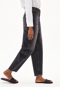 Jeans in denim nero a vita alta con taglio dritto, dotati di cinque tasche e cuciture visibili. Abbinati a sandali scivolati scuri.