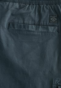 Dunkelgrauer Stoff mit matter Oberfläche, ausgestattet mit einem elastischen Bund und einer Gesäßtasche mit einem genähten Etikett.