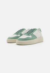 Grüne und weiße Sneakers mit einem Obermaterial aus Wildleder, perforierter Zehenbox, flachen Schnürsenkeln und einer robusten Gummisohle für zusätzlichen Halt.