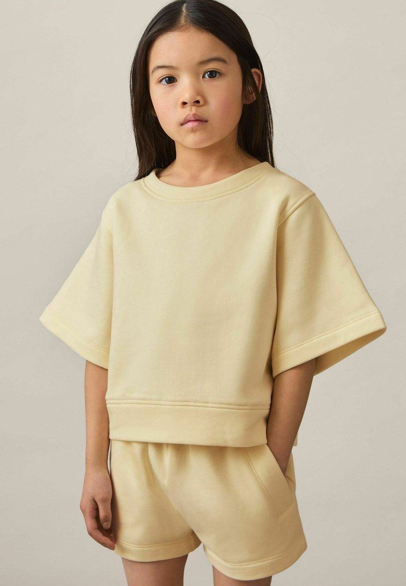 Lys gul bomuldsblandings sweatshirt med brede ærmer og rund hals, parret med matchende shorts, der har en afslappet pasform og struktureret stof.