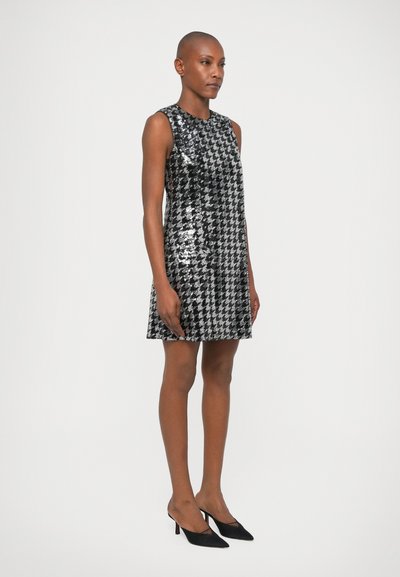 Μαύρο και ασημένιο φόρεμα με παγιέτες, διακοσμημένο με σχέδιο καρό, χωρίς μανίκια και φαρδιά κοπή, σε συνδυασμό με μαύρες γόβες με αιχμηρή μύτη.