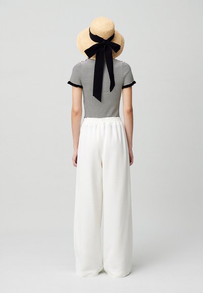 Top a rayas blanco y negro con mangas acampanadas, combinado con pantalones anchos crema. Sombrero de paja natural con cinta negra en la parte posterior.