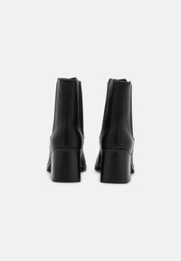 Černé kožené kotníkové boty se štíhlým designem, zaoblenou špičkou, vertikálním prošíváním a robustním středně vysokým podpatkem.