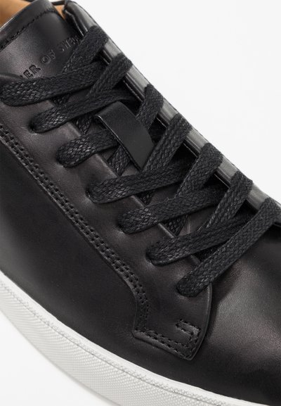 Sneaker in pelle nera con finitura testurizzata, dotato di lacci neri intrecciati, suola in gomma bianca e design minimalista.