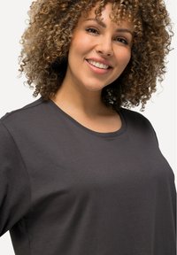 Maglietta scura grigia a maniche corte realizzata in morbido cotone. Presenta un collo rotondo e una vestibilità rilassata, con una texture liscia e dettagli minimali.