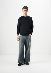 Pulover tricotat de culoare bleumarin cu Maneci lungi, asortat cu blugi deschiși cu croială largă și pantofi negri. Apariție simplă, casual, cu o croială lejeră.