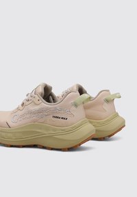 Baskets de sport beige avec une tige en maille texturée, des accents vert clair, des semelles épaisses et rembourrées, et un logo à motif sur le côté.