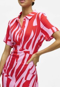 Vestido de manga corta en rojo y rosa, con un estampado rayado. Presenta un cierre de botones en la parte delantera y una cintura ajustada, fabricado con un tejido ligero.
