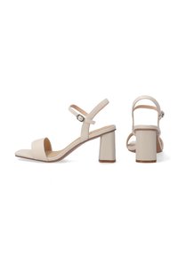 Beige sleehakken met een brede voorkantstrap, verstelbare enkelband, en een vierkante neus. Blokhakken zorgen voor stabiliteit.