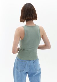 Canottiera a coste, senza maniche, in tessuto verde salvia; design aderente con scollatura alta, abbinata a jeans azzurri larghi.