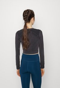 Svart, långärmad crop top med texturerad detaljering och logotyp på ärmarna, matchad med högmidjade, mörkblå leggings.