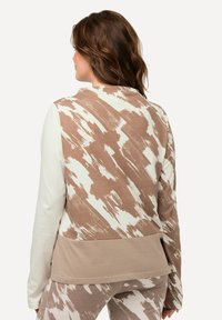 Beige und cremefarbener, gemusterter Langarmoberteil mit abgerundetem Saum, kontrastierenden Ärmeln und einer strukturierten Oberfläche mit abstrakten Pinselstrich-Designs.