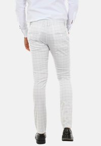 Pantaloni bianchi a scacchi con una vestibilità slim, realizzati in tessuto leggero. Sono dotati di tasche posteriori con bottoni e abbinati a scarpe nere.