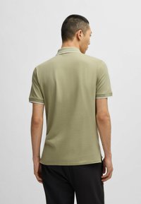 Khakifarbenes Poloshirt mit kurzen Ärmeln, geripptem Kragen und Bündchen mit weißen Akzenten, glatter Textur und seitlichen Schlitzen für einen bequemen Sitz.