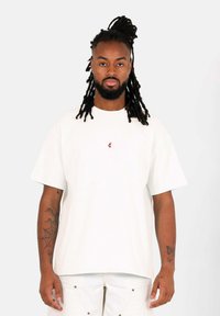 Vit bomulls t-shirt med avslappnad passform och korta ärmar, med en liten röd logotyp på bröstet och rak fåll.