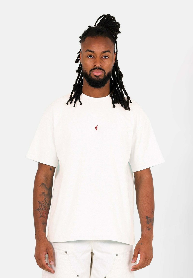 Vit bomulls t-shirt med avslappnad passform och korta ärmar, med en liten röd logotyp på bröstet och rak fåll.