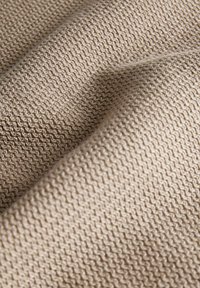 Tissu beige tricoté avec un motif zigzag texturé, présenté en gros plan avec des plis visibles et des ombres douces.