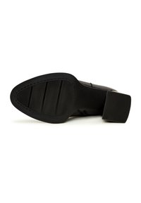 Vue de la semelle d'une chaussure noire à talon avec une semelle texturée et un talon carré épais sur fond blanc.