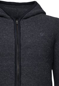 Sudadera con cremallera de color gris oscuro hecha de tela de punto texturizada. Presenta una capucha, un ribete en contraste de color azul marino oscuro y un pequeño logo bordado en el pecho.