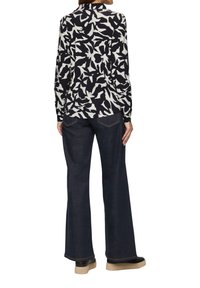 Langarm blouse in zwart-wit abstract patroon, gecombineerd met donkerblauwe wijde jeans. Textuurstof en zichtbare stikseldetails.