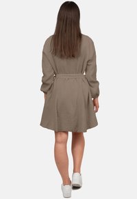 Abito taupe fino al ginocchio con un tessuto texturizzato e fluido, maniche lunghe e una cintura annodata in vita. Abbinato a sneaker bianche.