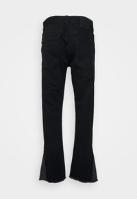 Jeans de mezclilla negra con bolsillos traseros, lazos para cinturón visibles y detalles de dobladillo sin acabar en la parte inferior.