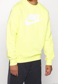 Gul sweatshirt i mjukt tyg med rund halsringning, prydd med en stor vit Nike-logga över framsidan och ribbade ärmslut och nederkant.