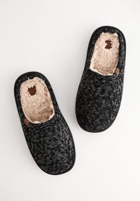 Chaussons noirs tricotés avec un motif texturé et une doublure en fourrure synthétique beige clair. Ils présentent une petite étiquette en cuir sur le côté et un design à bout rond.