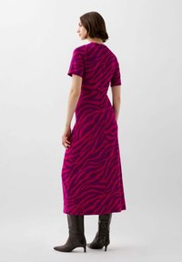 Fuchsia jurk met een gedurfde zebra-patroon, korte mouwen en een middenlengte, gecombineerd met zwarte kniehoge laarzen. Gladde textuur.