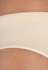 Fascia di intimo beige a costine con una texture morbida e liscia e una delicata rifinitura cucita lungo il bordo. Primo piano del materiale elastico.