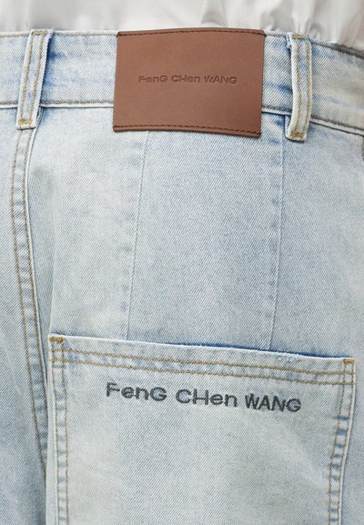 Φωτεινά γαλάζια τζιν με καφέ δερμάτινη ετικέτα στη μέση και κεντημένο όνομα μάρκας "Feng Chen Wang" στην πίσω τσέπη.