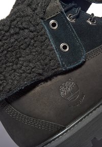 Bota negra impermeable con una parte superior texturizada de material suave, detalles de ante, ojales de metal y logotipo en relieve en el talón.
